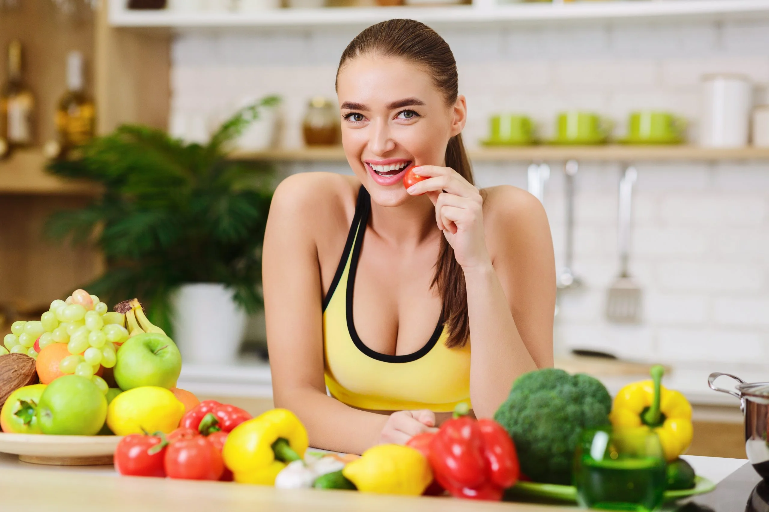 egy fiatal nő egy asztalnál ül, mosolyog, előtte zöldségek az asztalon